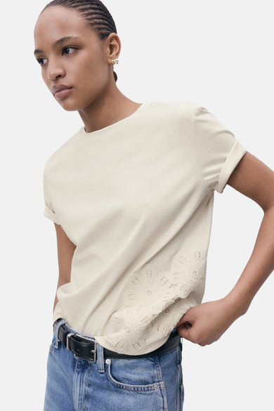 T-shirt beige à manches courtes de MANGO, fini avec des détails de bordure en bas, associé à un jean bleu.