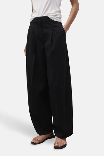 Pantalon de costume noir MANGO, avec des jambes larges, des plis à l'avant et porté avec des sandales.
