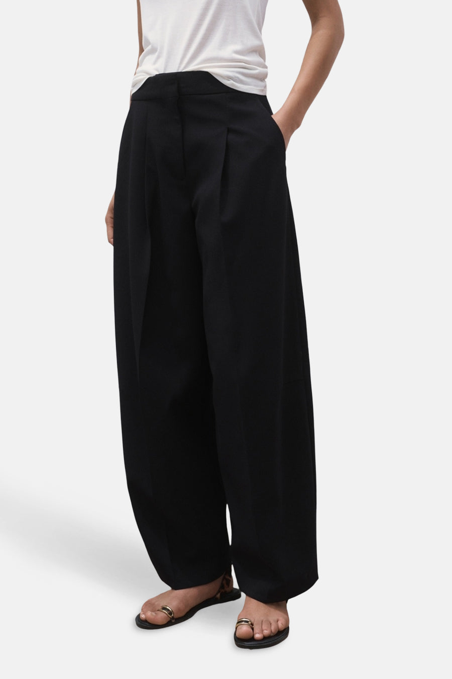 Pantalon de costume noir MANGO, avec des jambes larges, des plis à l'avant et porté avec des sandales.