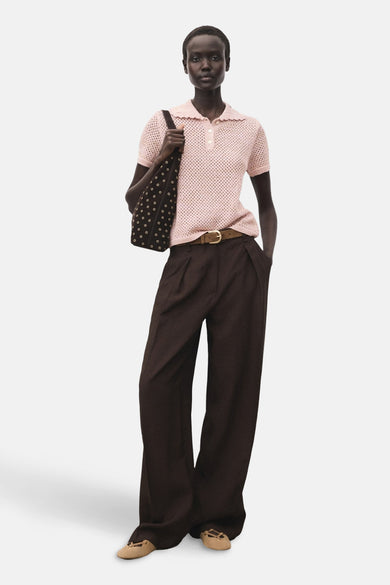 Roze polo met korte mouwen van MANGO, met opengebreide textuur en gedragen met bruine pantalon en tas.
