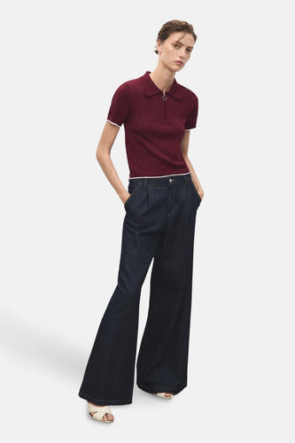 Bordeaux trui met ronde hals van MANGO, gecombineerd met donkere, uitlopende jeans en open schoenen.
