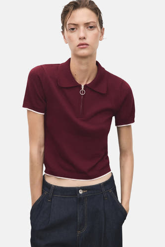Bordeaux trui met ronde hals van MANGO, met korte mouwen en een ritssluiting aan de voorkant, gecombineerd met donkere jeans.
