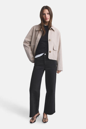 Jean en denim noir large de MANGO, associé à une veste beige et un haut noir, avec des sandales.