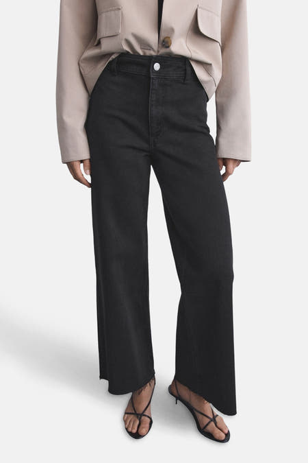 Zwarte wijde jeans van MANGO, gecombineerd met een beige jasje en strappy sandalen.