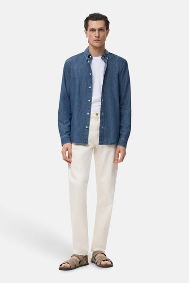 Denim overhemd met lange mouwen van MANGO, gedragen over een wit T-shirt en gecombineerd met crèmekleurige broek en bruine sandalen.
