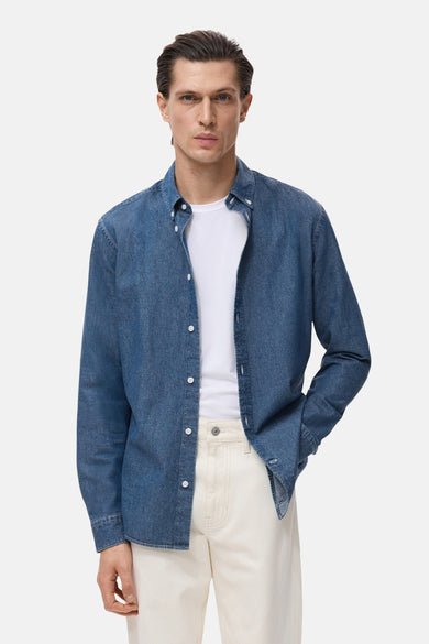 Denim overhemd met lange mouwen van MANGO, gedragen over een wit T-shirt en crèmekleurige broek.