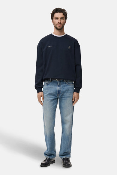 Blauwe sweater van MANGO, met kleine logo op de borst, gecombineerd met jeans en leren schoenen.