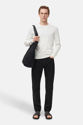 Jean noir droit de MANGO, associé à une chemise blanche et des sandales noires, avec un sac sur l'épaule.
