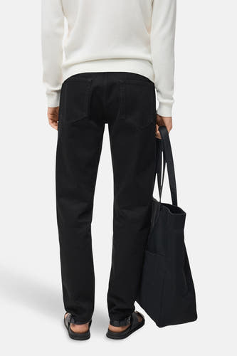 Jean droit noir en denim de MANGO, avec l'arrière visible, associé à une chemise blanche et des sandales noires et un sac.
