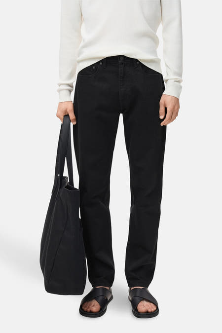 Jean droit noir de MANGO, porté avec une chemise blanche et des sandales noires, et avec un sac noir.