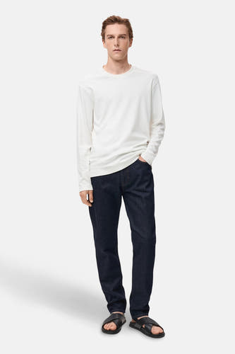 Donkerblauwe rechte jeans van MANGO, gecombineerd met een wit shirt met lange mouwen en zwarte sandalen.