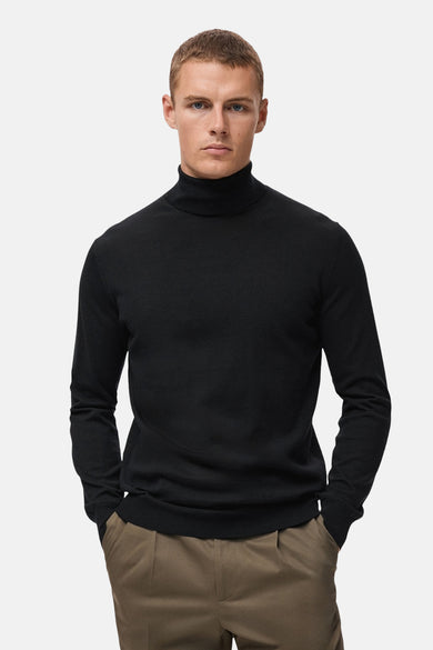 Pull noir avec col rond de MANGO, porté avec un pantalon kaki.