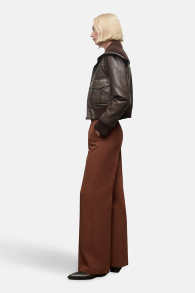 Bruine broek van MANGO, wijde pijpen, met een hand in de zak, gecombineerd met een leren jas.