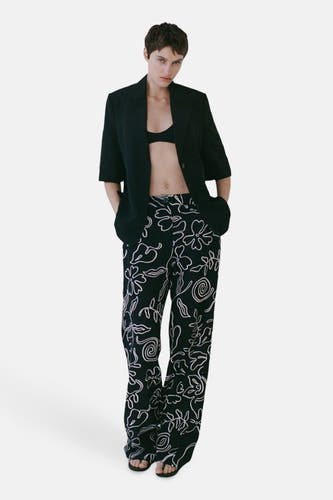 Pantalon noir de MANGO, avec une impression florale blanche et porté avec un blazer noir et un haut.