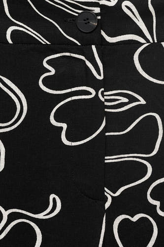 Pantalon noir de MANGO avec une impression de fleurs blanches et une fermeture à bouton, en vue rapprochée.