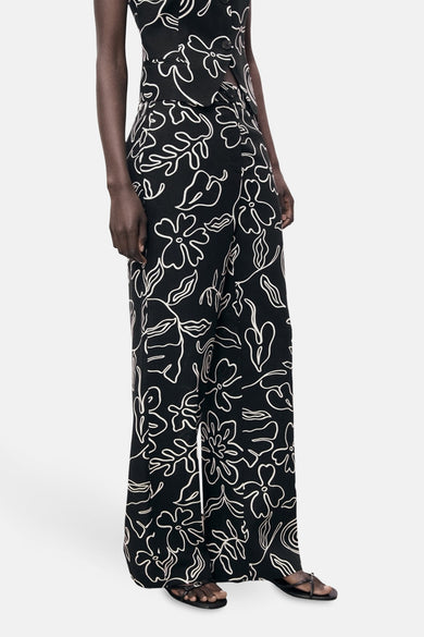 Pantalon noir de MANGO avec un motif floral blanc, des jambes largement évasées et des sandales.