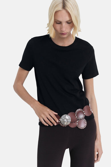 T-shirt noir à manches courtes de MANGO, porté avec une large ce ce décorée d'accentuations argentées et un legging marron.