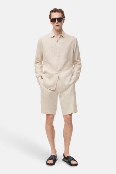 Beige overhemd met lange mouwen van MANGO, gedragen met een bijpassende korte broek en zwarte sandalen.
