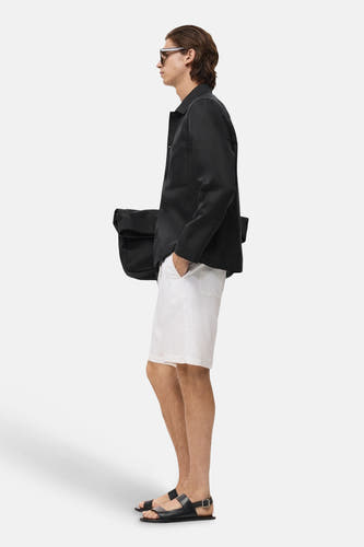 Zwarte korte jas van MANGO, gedragen met een witte korte broek en zwarte sandalen, zijaanzicht.
