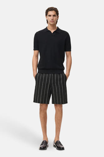 Zwarte short van MANGO, met krijtstrepen en steekzakken, gecombineerd met een zwart poloshirt en leren loafers.