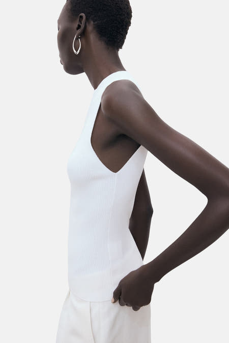 Witte singlet van MANGO, gedragen met crèmekleurige broek en zilveren oorringen, zijaanzicht.
