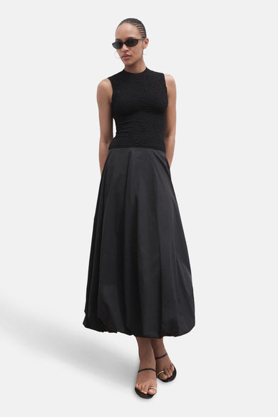 Blouse sans manches noire de MANGO, avec une subtile texture et associée à une longue jupe noire.