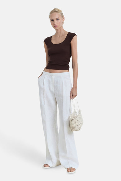 T-shirt sans manches marron de MANGO, porté avec un pantalon de lin blanc et une sac en tricot.