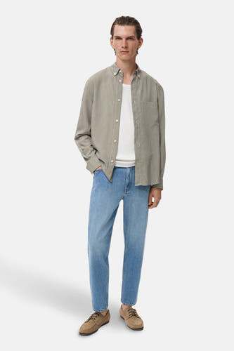 Kaki overhemd met lange mouwen van MANGO, gedragen over een wit T-shirt en gecombineerd met blauwe jeans.
