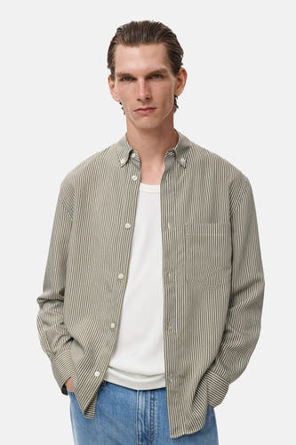 Kaki overhemd met lange mouwen van MANGO, met strepen en een borstzak, gedragen over een wit T-shirt.
