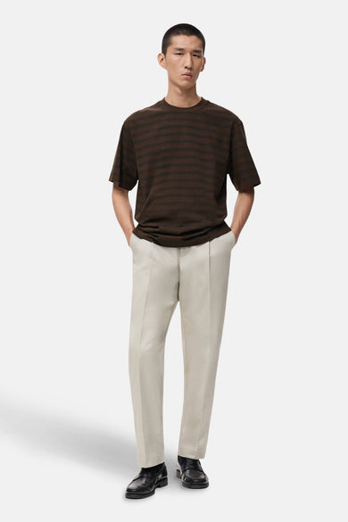 T-shirt rayé brun avec manches courtes de MANGO, porté avec un pantalon crème et des loafers en cuir noirs.