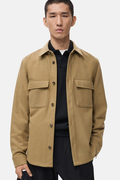 Manteau court marron de MANGO avec poches poitrine, porté sur une polo noire et un pantalon noir.