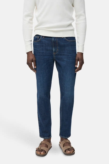 Jean tapered bleu marine de MANGO, porté avec un pull blanc et des sandales brunes.