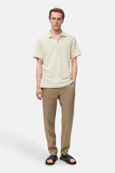 Polo écru à manches courtes de MANGO, porté avec un pantalon de lin marron et des sandales noires.