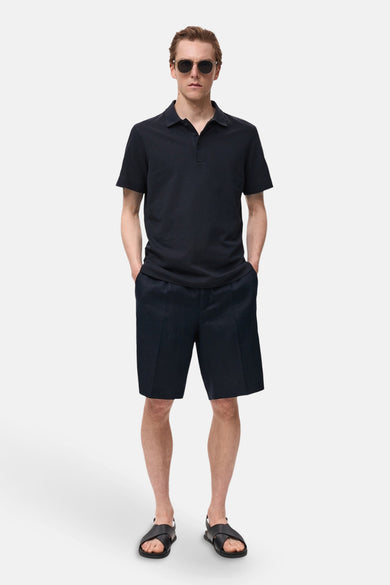 Polo bleu marine à manches courtes de MANGO, porté avec des shorts et des sandales en cuir.