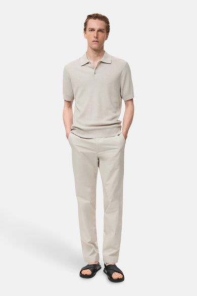 Polo écru à manches courtes de MANGO, avec une texture rayée, associé à un pantalon beige clair et des sandales noires.