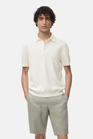 Polo écru à manches courtes de MANGO, porté avec des shorts en lin verts.