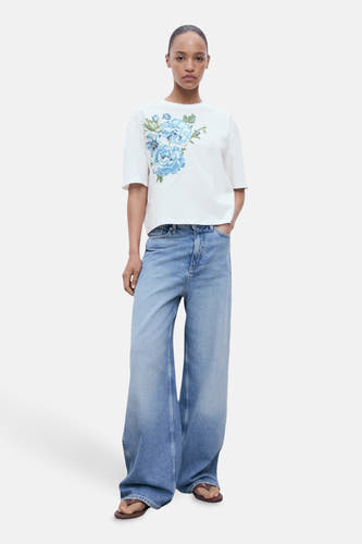 T-shirt multicolore (manches courtes) de MANGO, avec une impression de fleurs bleues, associé à des jeans larges et des sandales.
