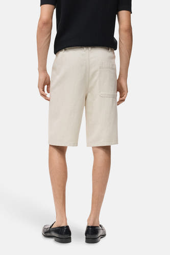 Jeansshort in ecru van MANGO, met een zak aan de achterkant en gedragen met zwarte loafers.
