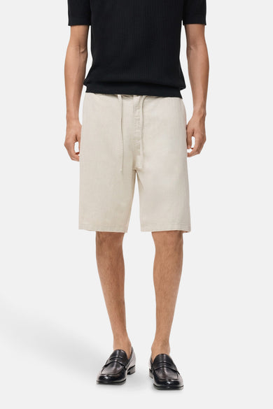 Jean écru court de MANGO, avec cordon de serrage et porté avec un t-shirt noir et des mocassins en cuir.
