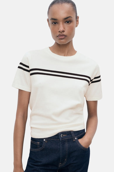 T-shirt blanc à manches courtes de MANGO, avec une double bande noire sur la poitrine, associé à des jeans foncés.