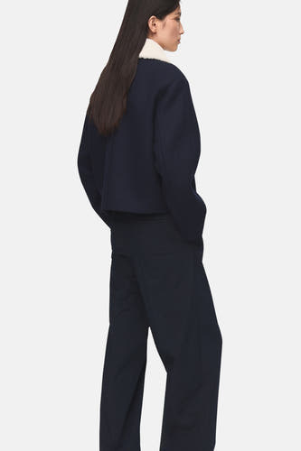 Blauwe korte jas van MANGO, gezien van achteren, met een witte kraag en donkerblauwe broek.