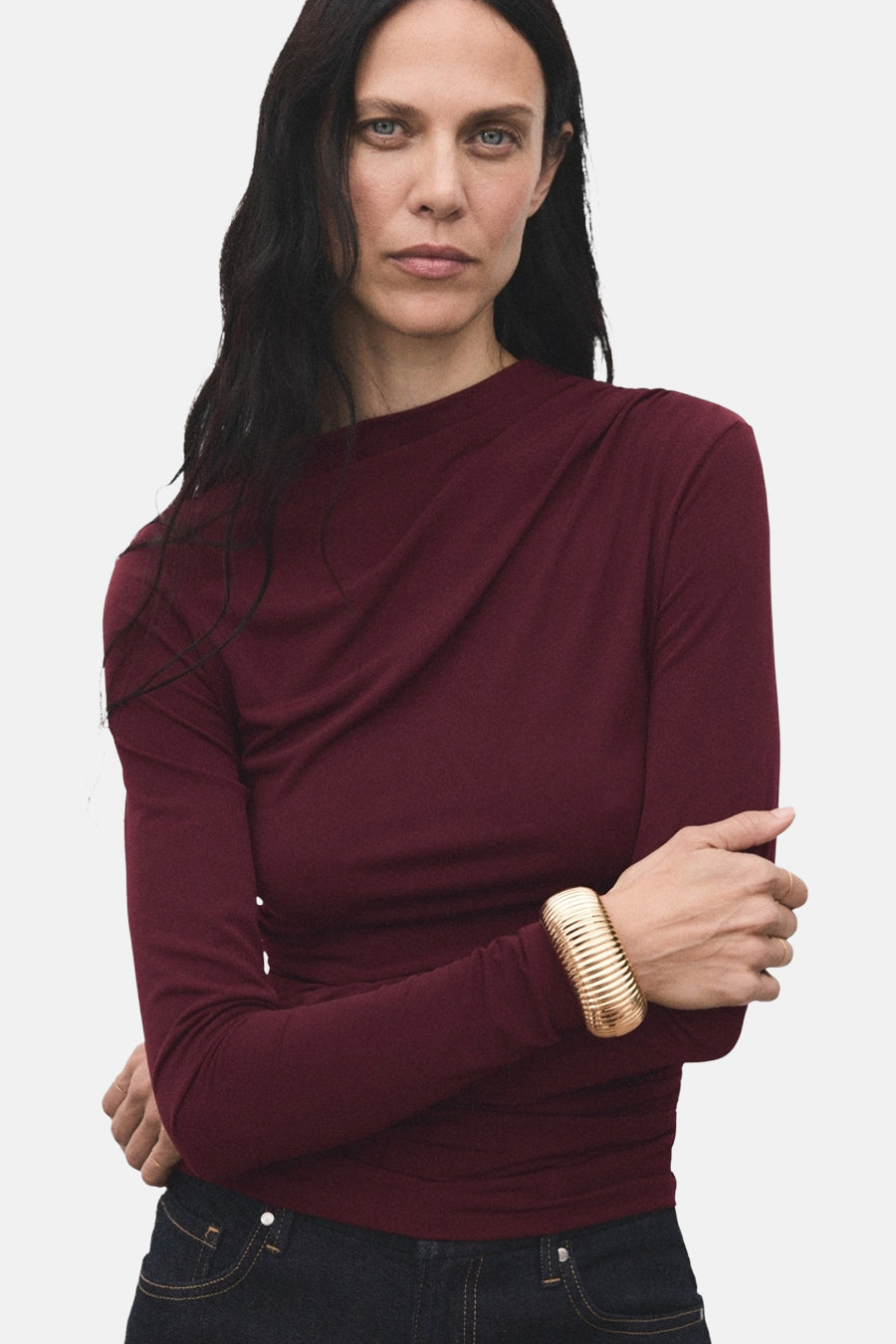 Bordeauxkleurige T-shirt met lange mouwen van MANGO, met een gedrapeerde halslijn en gecombineerd met een gouden armband.
