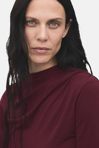 Bordeaux T-shirt met lange mouwen van MANGO, gedrapeerde halslijn, gedragen door een vrouw.
