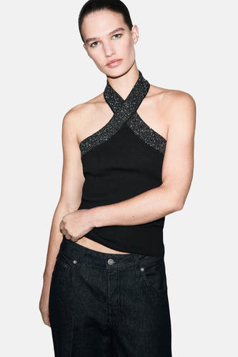 Zwarte mouwloze blouse van MANGO, met gekruiste halsband versierd met pailletten, gecombineerd met donkere jeans.
