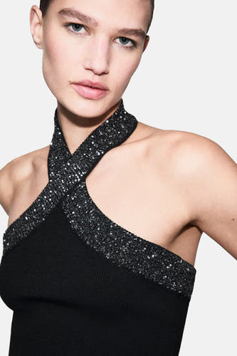 Zwarte mouwloze blouse van MANGO, met gekruiste glitterbandjes en een ribgebreide textuur.
