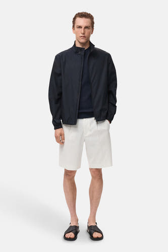 Korte blauwe jas van MANGO, met een ritssluiting, gedragen met een donkerblauwe trui en gestreepte shorts.
