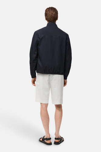 Korte blauwe jas van MANGO, gezien van achteren, gedragen met gestreepte shorts en sandalen.

