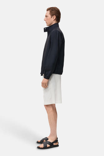 Blauwe korte jas van MANGO, gedragen met gestreepte shorts en leren sandalen, zijaanzicht.
