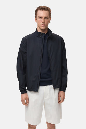 Korte blauwe jas van MANGO, gedragen met een donkerblauwe trui en gestreepte witte shorts.