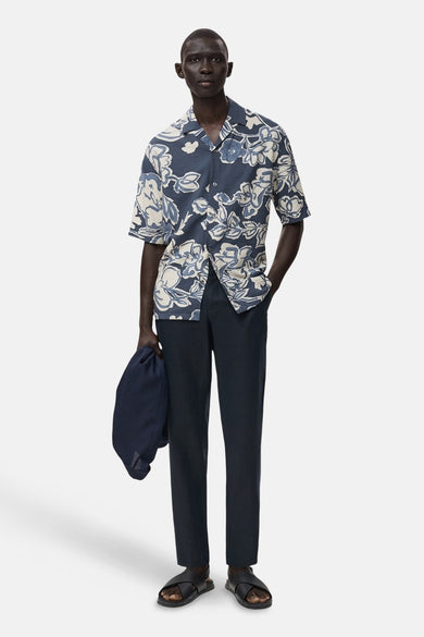 Blauwe broek van MANGO, gecombineerd met een bloemen overhemd, sandalen en een tas.
